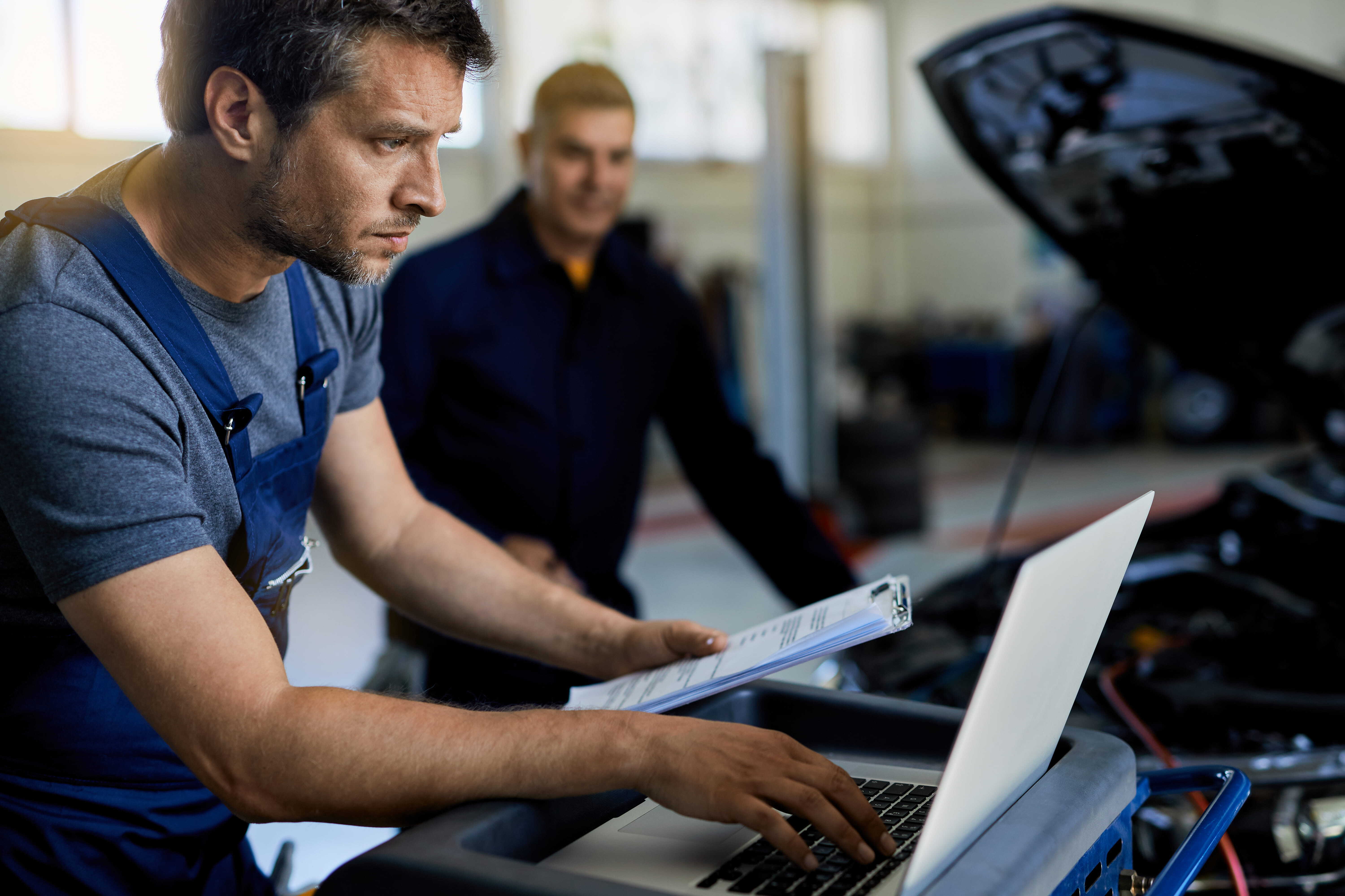 Mechanic is looking at a laptop which is connected to a car diagnostic machine which is hooked up to a car