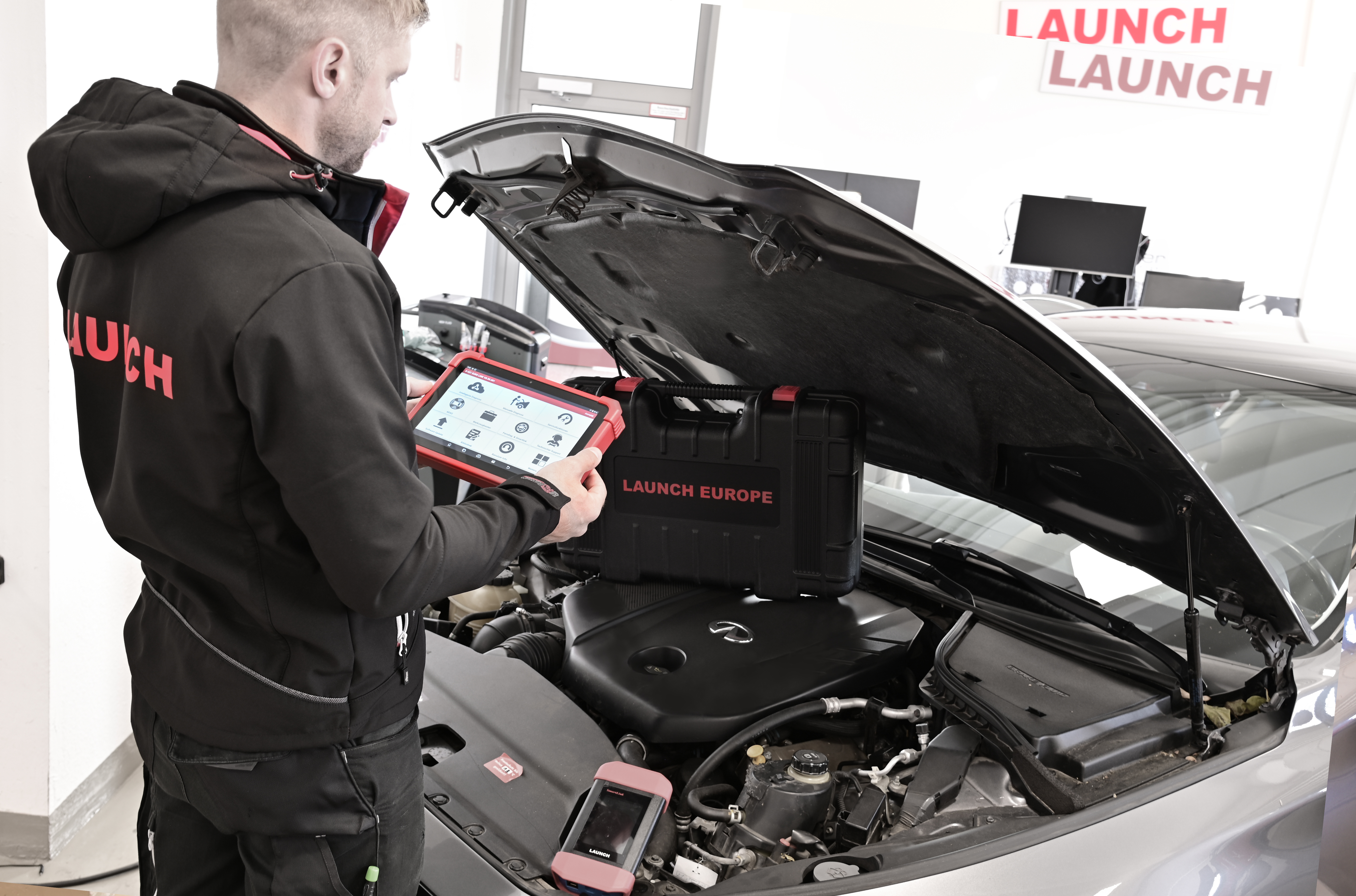 Technician using a Launch diagnostic tablet under the bonnet of a vehicle, carrying out DPF diagnostics alongside professional cleaning equipment.